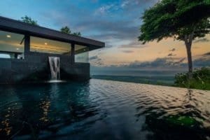 Modern home with infinity pool and panoramic ocean view at sunset.