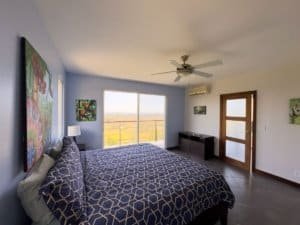 Bright bedroom with large window overlooking scenic ocean and mountain views.