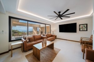Spacious living room with large window showing ocean and jungle view, modern decor, ceiling fan.