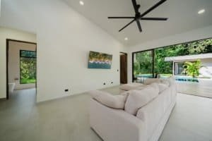 Contemporary living room with large glass doors overlooking pool and lush greenery.