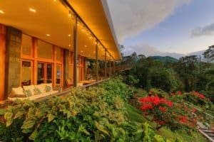 Modern mountain home with large glass windows and lush garden landscape.