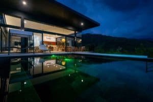 Modern luxury home with infinity pool and mountain view at night.