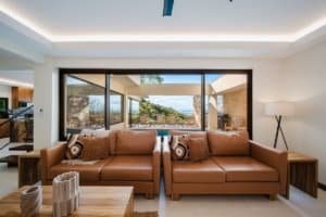 Modern living room with large windows overlooking ocean and jungle scenery.