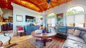 Bright living room with high wooden ceiling, large windows, and tropical decor.