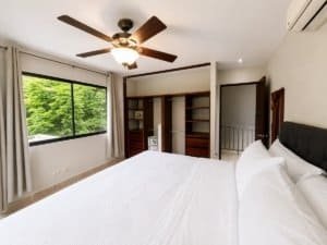 Bright bedroom with large window, ceiling fan, and garden view in Dominical.