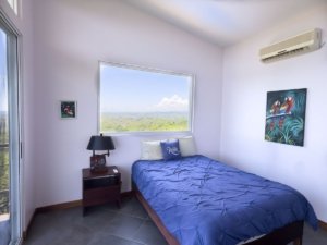 Bedroom with large window overlooking lush landscape and ocean in Dominical.