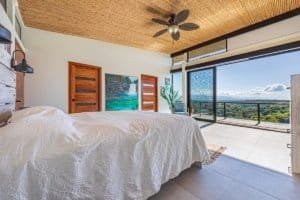 Modern bedroom with large glass doors overlooking lush mountain scenery in Dominical.