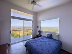 Bedroom with large windows showing panoramic ocean and mountain views in Dominical.