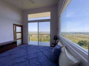 Bedroom with large windows showing ocean, mountain, and sunset views in Dominical.