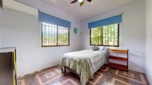 Bright bedroom with two windows, single bed, and wooden furniture in Dominical.