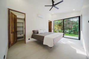 Bright bedroom with large glass door overlooking lush garden.