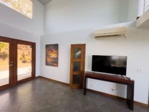 Bright living room with large windows, TV, and wooden door in Dominical.