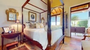 Luxurious bedroom with four-poster bed and balcony view of lush greenery.