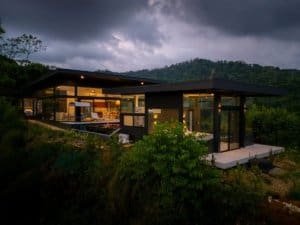 Modern house with large glass windows overlooking lush green landscape and mountains.