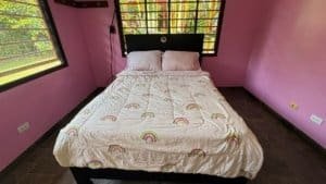 Comfortable bedroom with rainbow-themed bedding and pink walls in Dominical.
