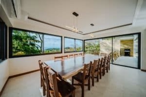Modern dining room with large windows overlooking lush jungle and ocean scenery.