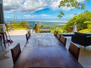 Stunning ocean view from a terrace with dining area and lush greenery.