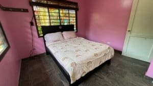 Bedroom with pink walls, black bed frame, and rainbow-themed bedding in Dominical.
