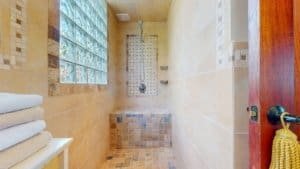 Modern walk-in shower with beige tiles and glass block window in tropical home.