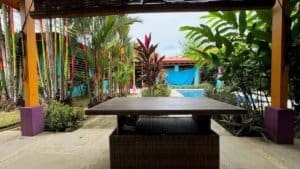 Covered outdoor dining space with tropical plants and garden view.