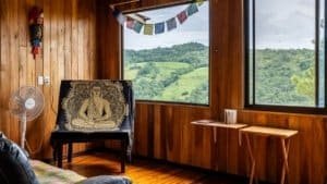 Interior of a mountain home with wooden walls and large windows showing lush green hills.