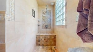 Modern bathroom with stone tiles, glass block window, and walk-in shower.