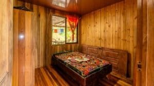 Interior of a wooden mountain home bedroom with colorful bedspread and window view.