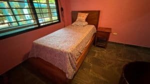 Single bed in a simple bedroom with pink walls and window view of greenery.