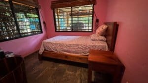 Bedroom with pink walls, wooden furniture, and large windows in Dominical.