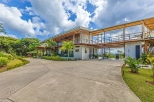 Modern estate with expansive balcony, lush gardens, and mountain backdrop.