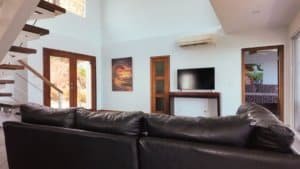 Spacious living room with black leather sofa, TV, and mountain views in Dominical.