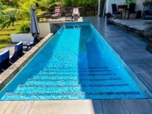 Modern swimming pool with ocean view, outdoor lounge, and lush greenery.