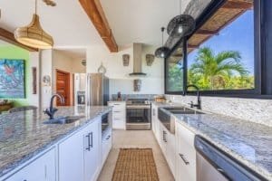 Bright kitchen with mountain views, white cabinets, granite countertops, and tropical decor.
