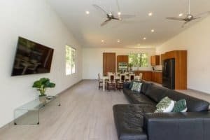Spacious living room with black sofa, wall-mounted TV, and large windows showing mountain scenery.