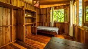 Interior of a wooden mountain home bedroom with large windows and natural light.