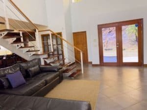 Spacious living room with black leather sofa and large glass doors showing mountain scenery.