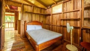 Interior of a rustic bedroom with wooden walls, bed, and fan near Nauyaca Waterfalls.