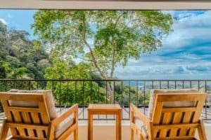 Balcony with two wooden chairs overlooking lush jungle and ocean view.