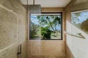 Modern bathroom with large window overlooking lush jungle and ocean view.