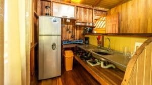 Small rustic kitchen with fridge, sink, and wooden cabinets near Nauyaca Waterfalls.