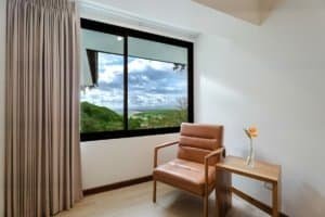 Interior of a room with a large window showing ocean and jungle view, beige armchair, and side table.