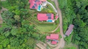 Aerial view of a tropical estate with pool, solar panels, and ocean in background.