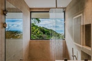 Modern bathroom with large window overlooking lush jungle and ocean scenery.