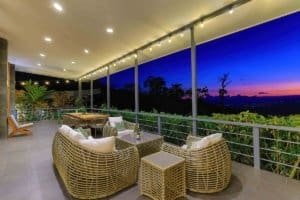 Spacious balcony with wicker furniture overlooking lush mountains at sunset.