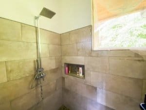 Bathroom with beige tiles, shower, and window overlooking greenery.