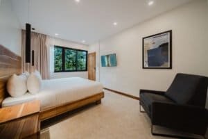 Modern bedroom with jungle view, minimalist decor, and black armchair.