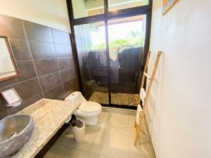 Bathroom with stone sink, toilet, and ocean view through glass door.