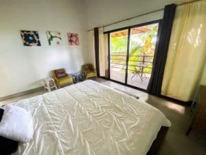 Bedroom with balcony overlooking lush tropical landscape and ocean view.