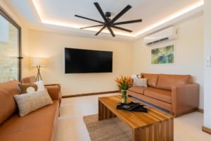 Modern living room with leather sofas, flat-screen TV, and rainforest view.