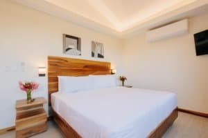 Modern bedroom with wooden accents, white bedding, and tropical decor.
